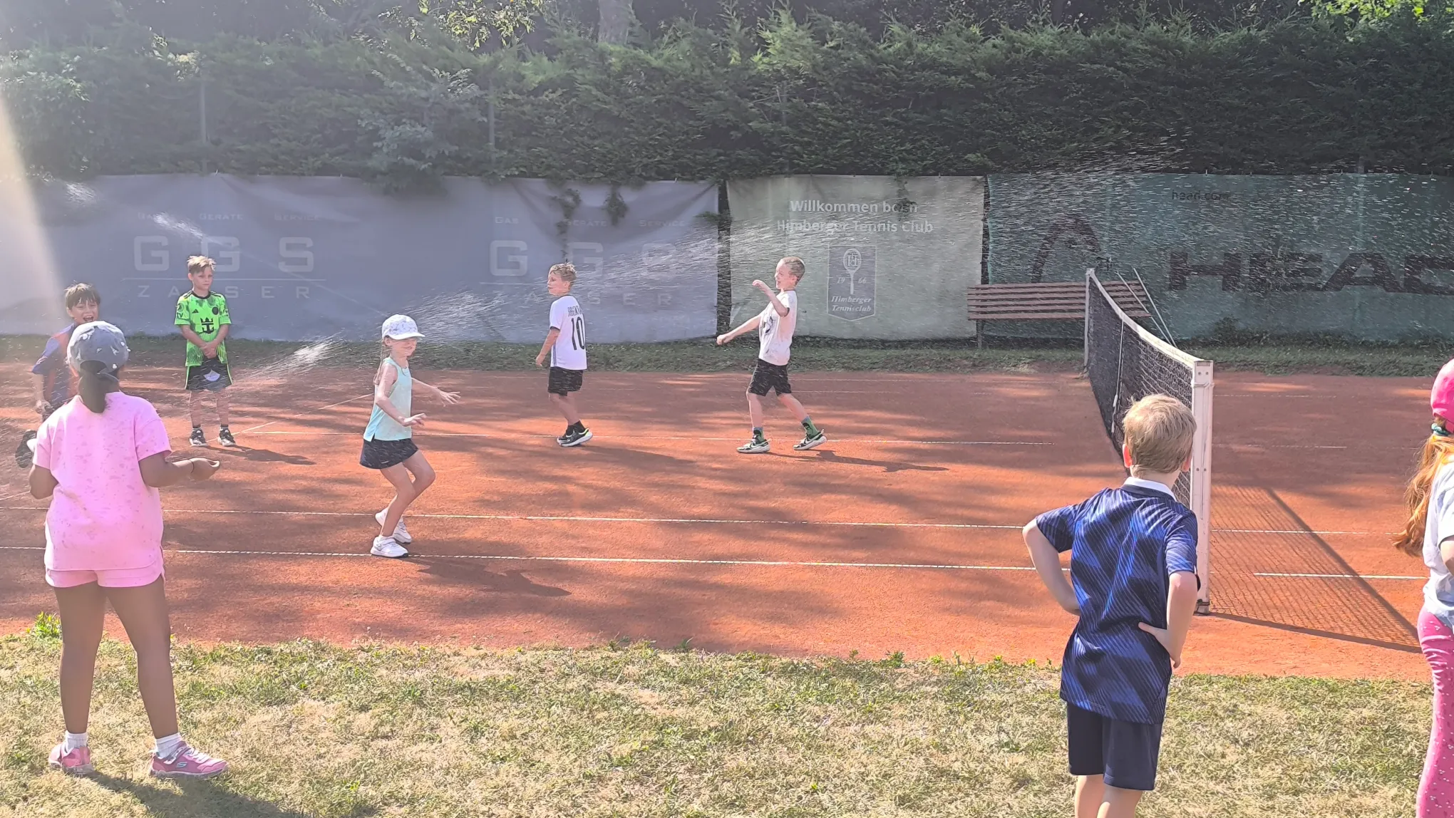 Kinder haben Spaß beim Tenniscamp mit Wassersprenger am Platz