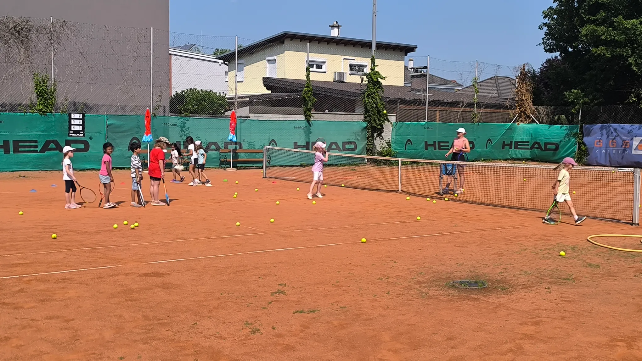 Kinder üben Tennis mit Trainerin auf der Tennisanlage