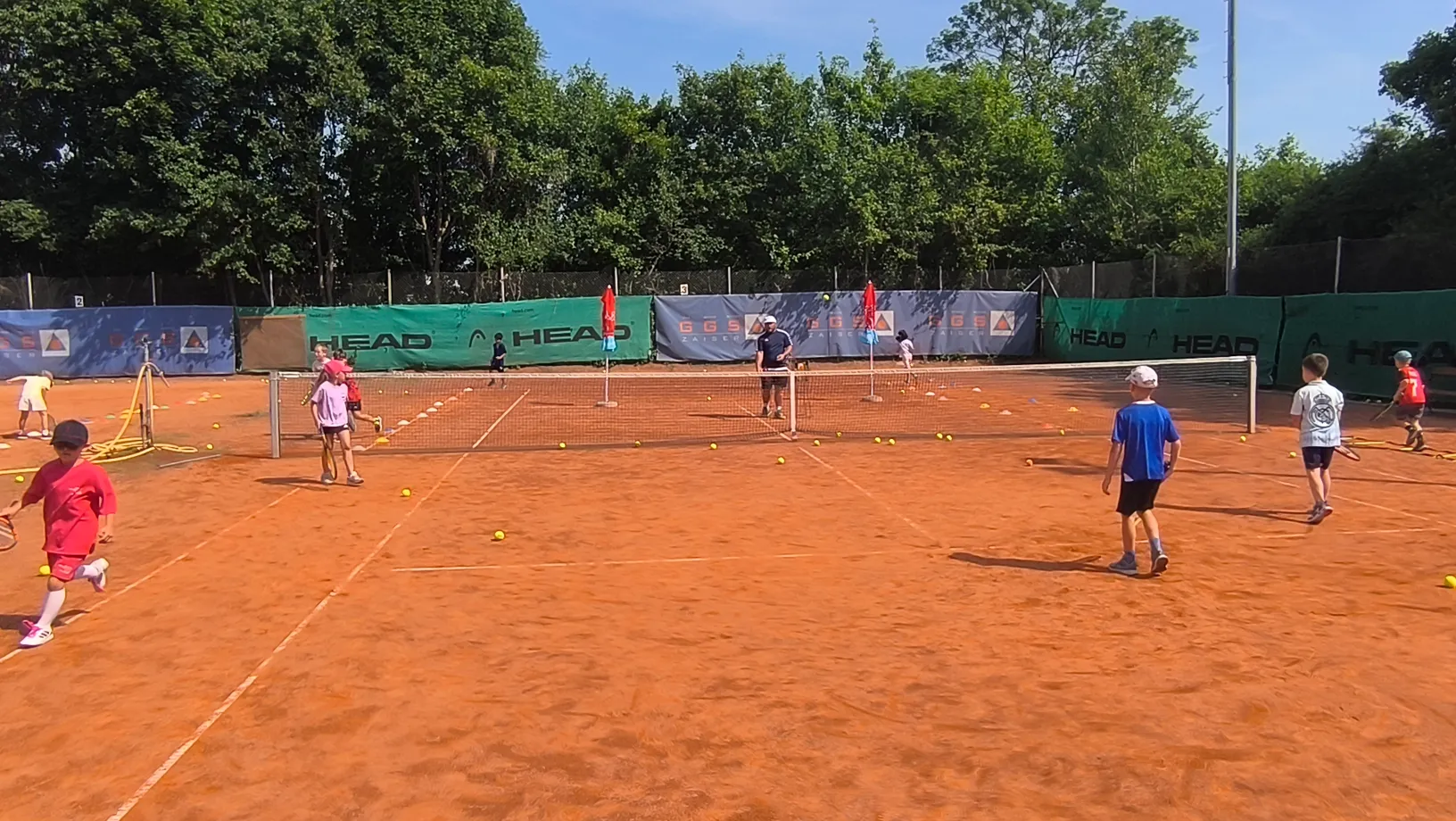 Kinder üben Tennis mit Trainer auf der Tennisanlage