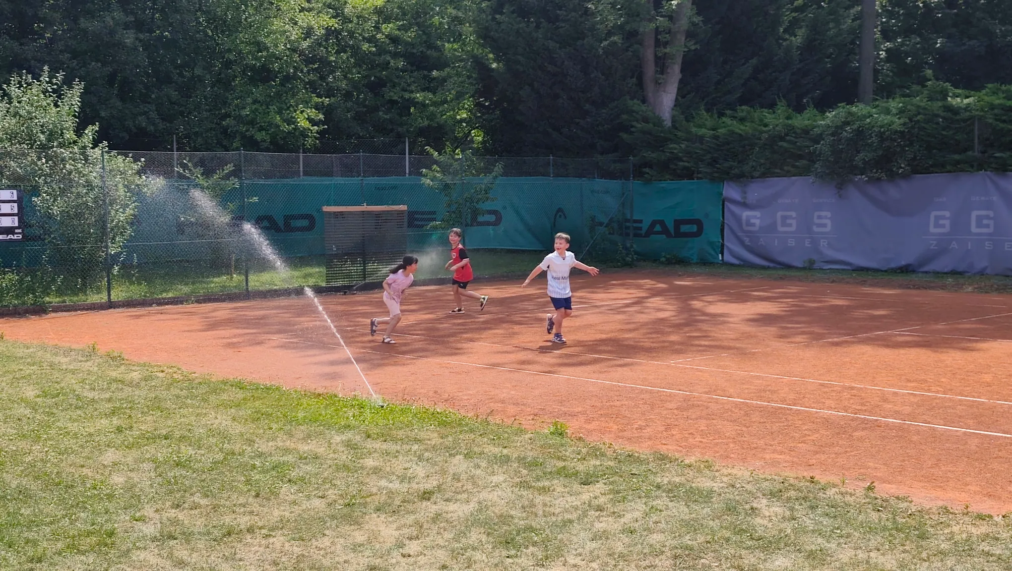 Kinder haben Spaß beim Tenniscamp mit Wassersprenger am Platz