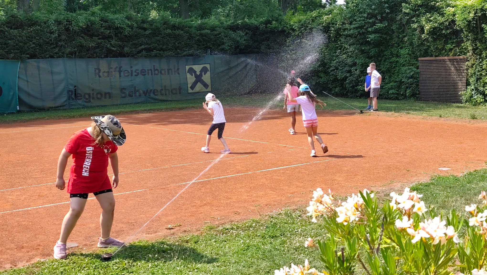 Kinder haben Spaß beim Tenniscamp mit Wassersprenger am Platz