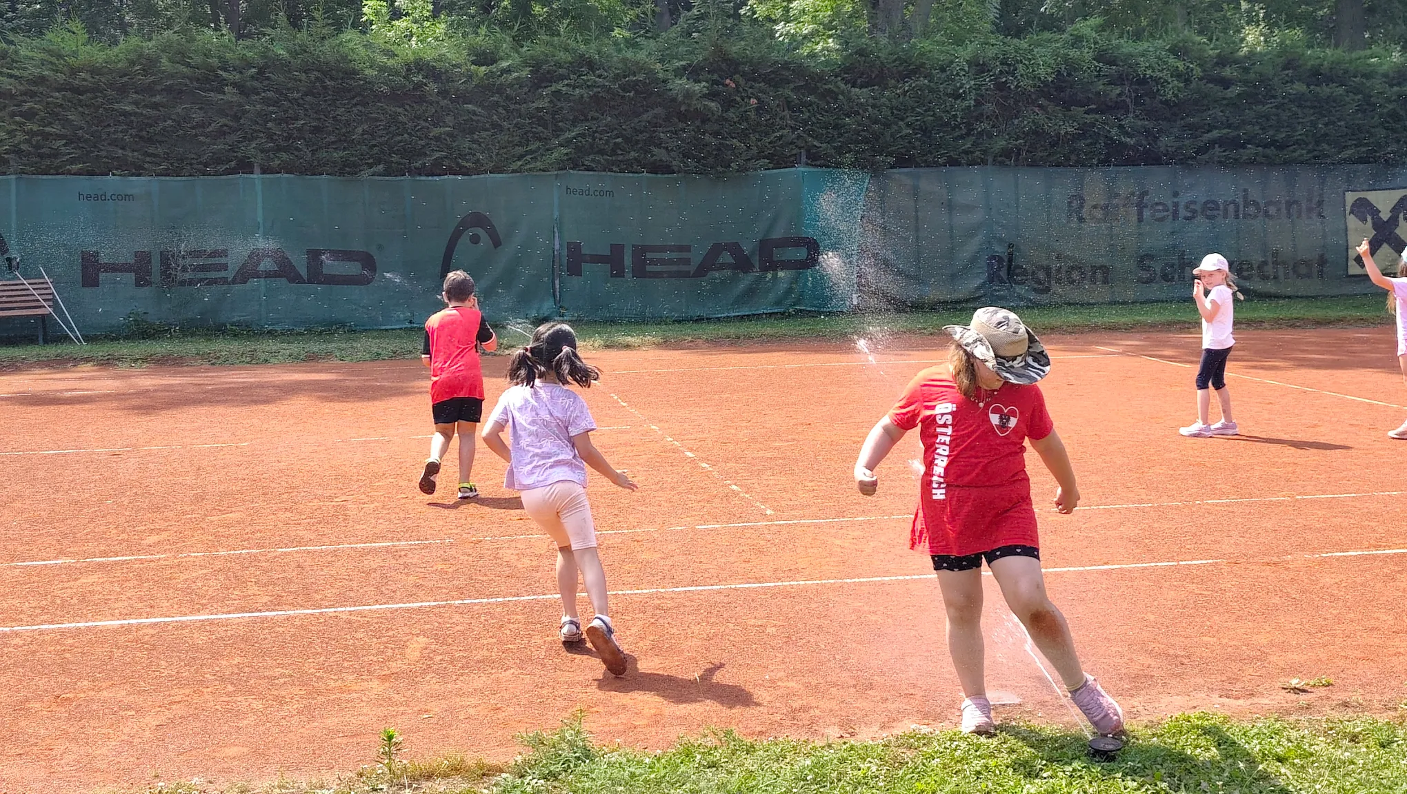 Kinder haben Spaß beim Tenniscamp mit Wassersprenger am Platz