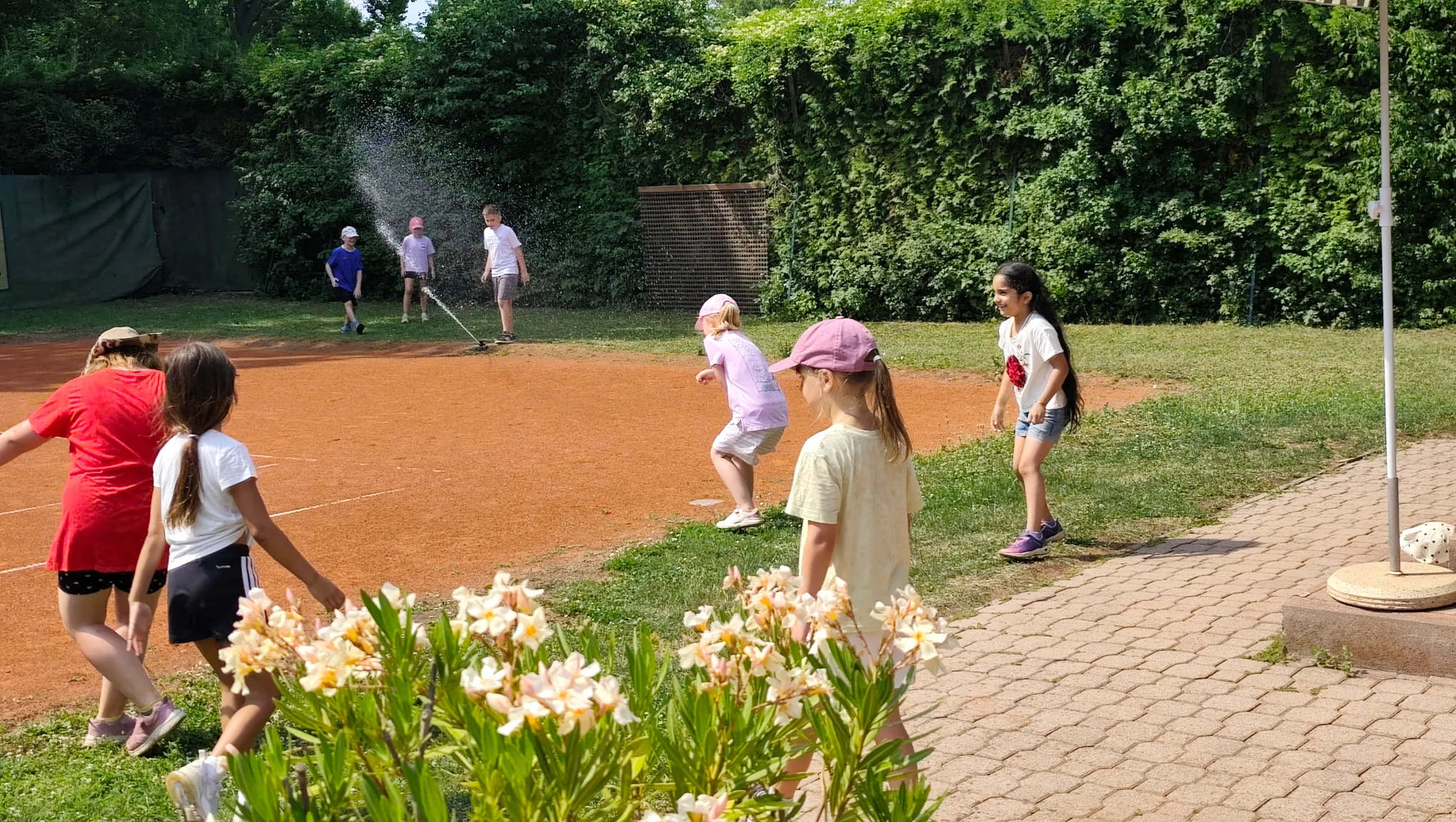 Kinder haben Spaß beim Tenniscamp mit Wassersprenger am Platz