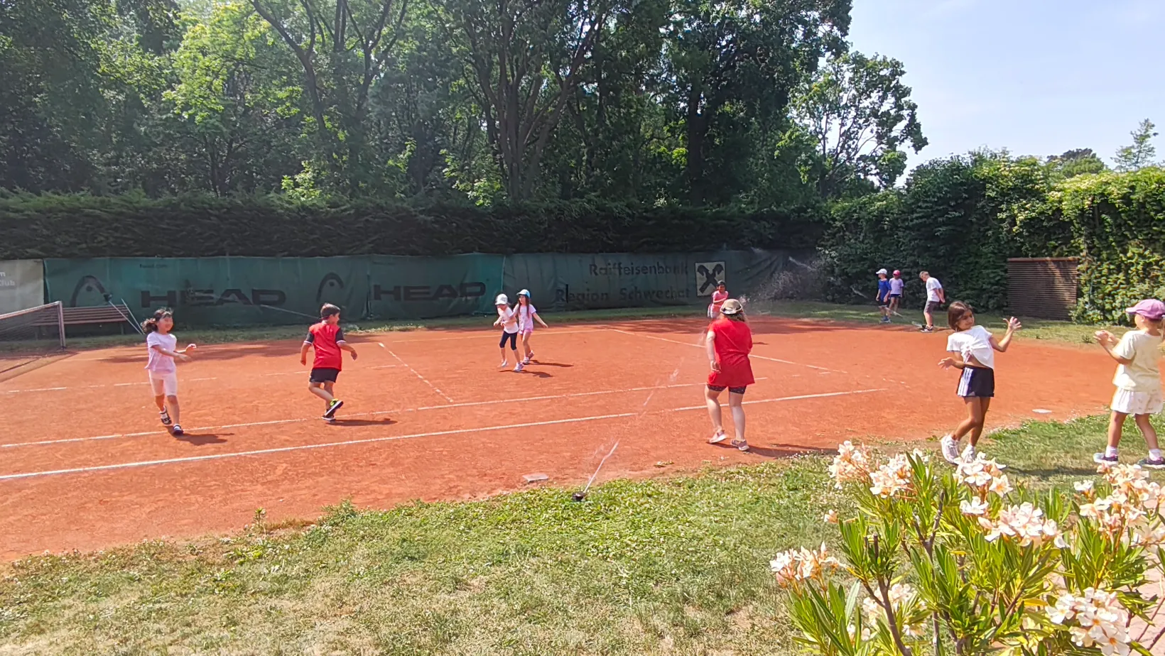 Kinder haben Spaß beim Tenniscamp mit Wassersprenger am Platz