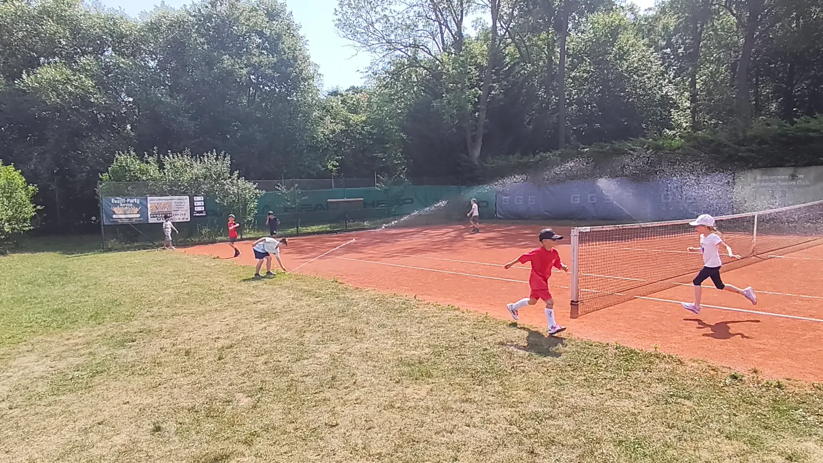 Kinder haben Spaß beim Tenniscamp mit Wassersprenger am Platz