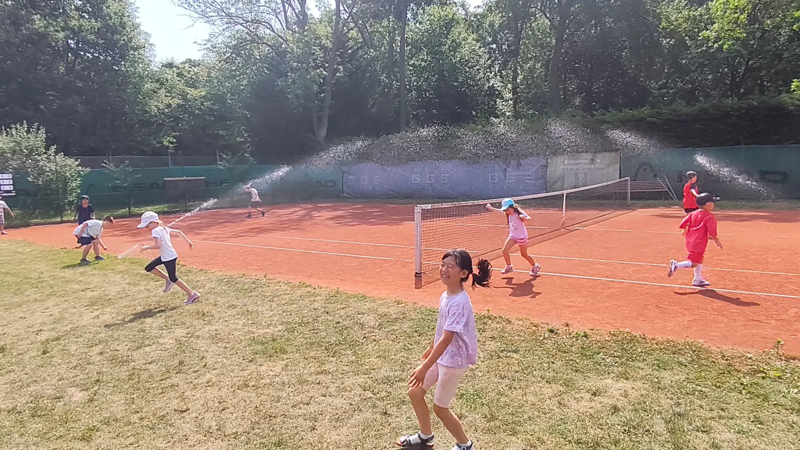 Kinder haben Spaß beim Tenniscamp mit Wassersprenger am Platz