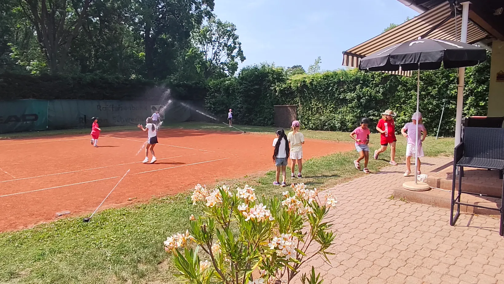 Kinder haben Spaß beim Tenniscamp mit Wassersprenger am Platz