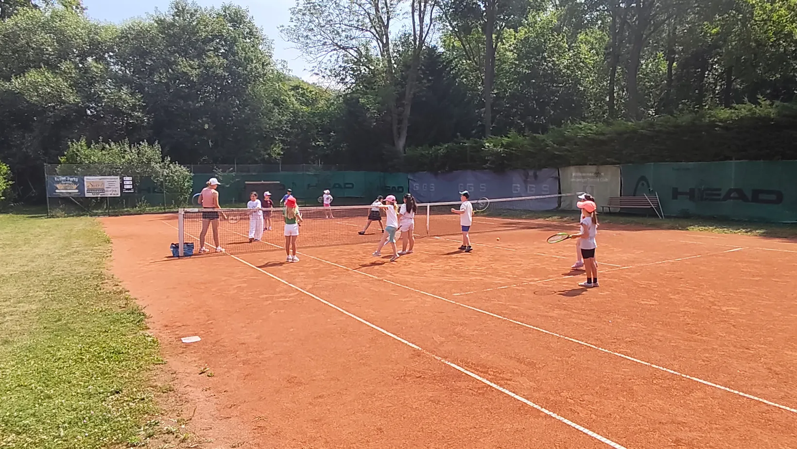 Kinder üben Tennis mit Trainerin auf der Tennisanlage